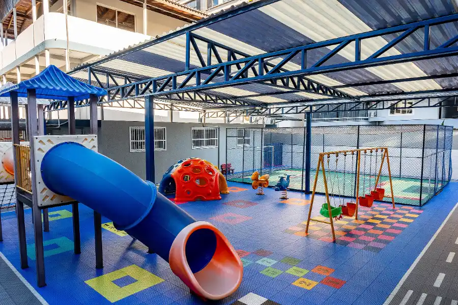 Parque infantil coberto do Colégio Atlântico com escorregador, balanços e brinquedos coloridos, espaço de recreação para alunos da Educação Infantil.