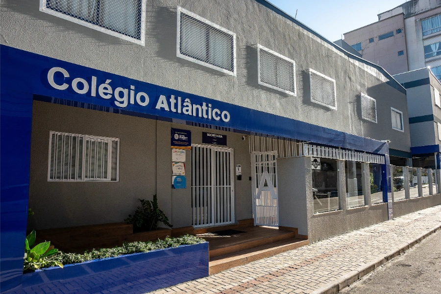 Fachada principal do Colégio Atlântico em Itapema, com entrada da secretaria e letreiro azul em destaque.